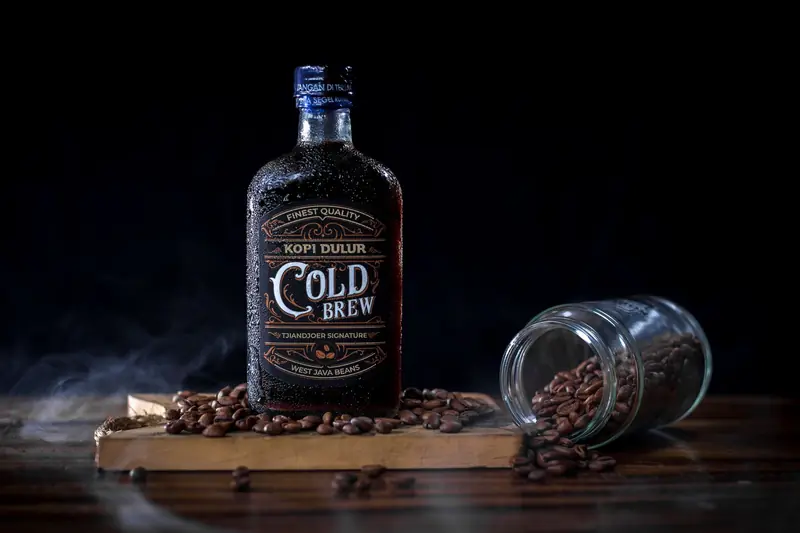 A cold brew coffee bottle with West Java beans, surrounded by scattered coffee beans
