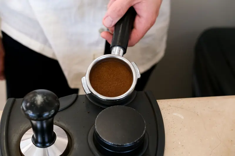 Close-up of a barista preparing espresso, showcasing the portafilter and tamper