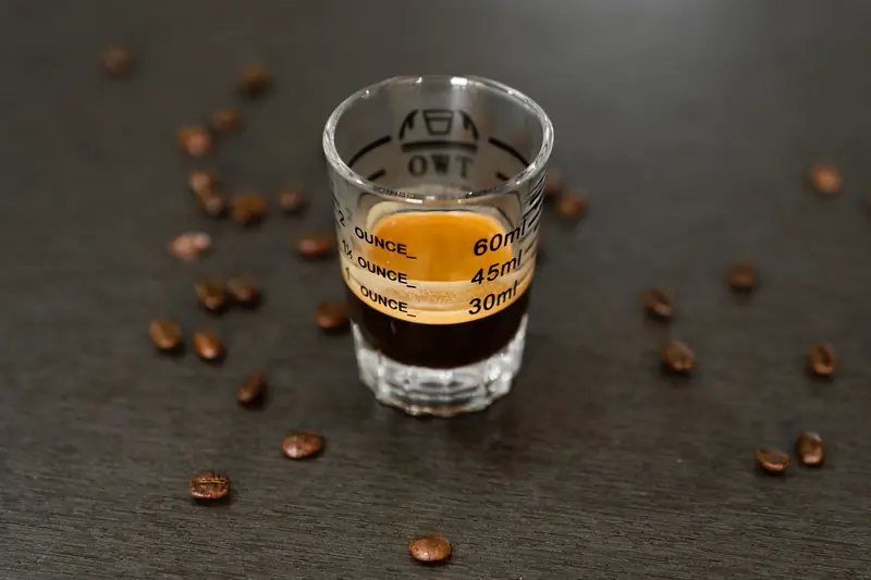 A rich espresso shot in a measuring glass surrounded by scattered coffee beans, perfect for coffee lovers