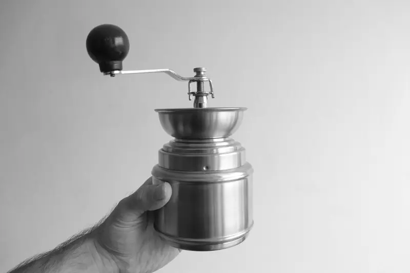 Classic black and white image of a hand holding a metal coffee grinder