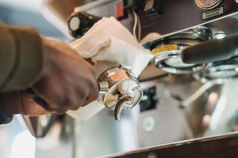 Close-up of barista cleaning a coffee machine portafilter with cloth for hygiene