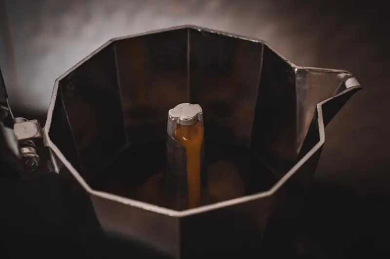 A detailed view of espresso brewing in a steel Moka pot, capturing rich coffee textures