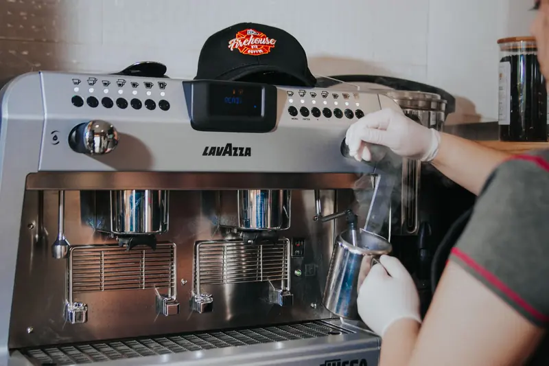 Barista steaming milk with Lavazza espresso machine, indoors, wearing gloves