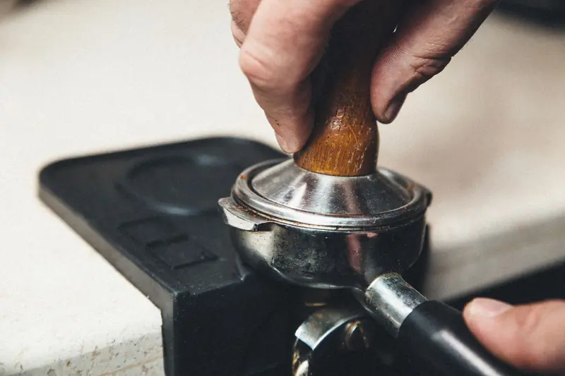 Detailed view of a barista using a tamper on a portafilter for espresso preparation