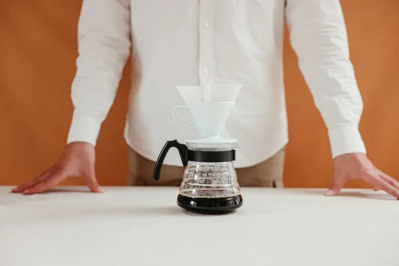 A person makes pour over coffee using a dripper, perfect for coffee enthusiasts