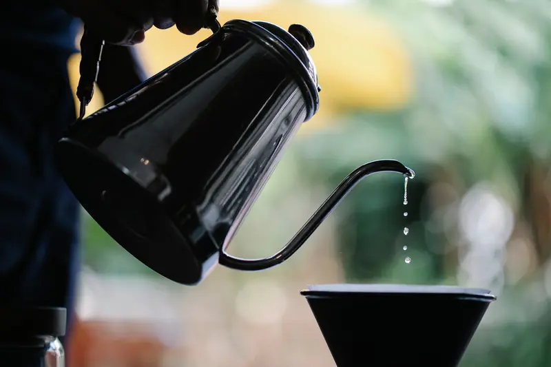 Crop anonymous person pouring water into cup with paper filter while preparing alternative coffee on terrace overlooking green garden