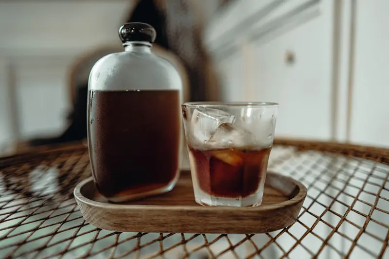Glass of cold brew coffee with ice cubes on a rustic tray indoors