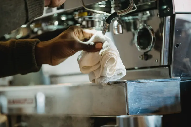 Close-up of a person cleaning a coffee machine using a cloth. Focus on hygiene and maintenance