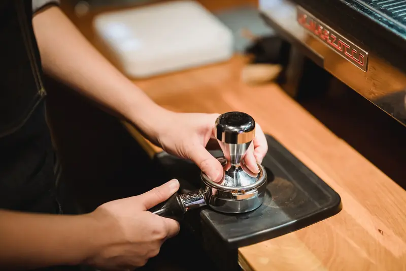 Close-up of barista hands tamping espresso grounds using a portafilter in a cozy café setting