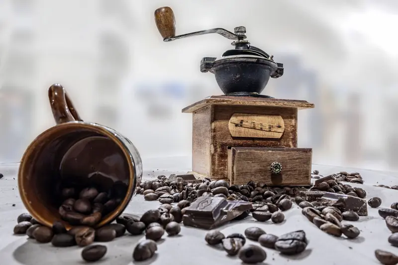 Wooden coffee grinder with beans and chocolate on a rustic table setting