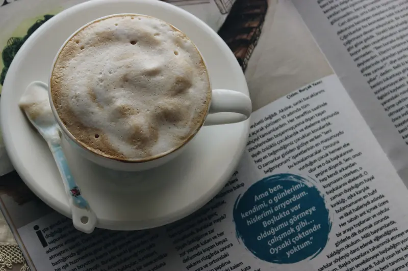 A steaming cappuccino with thick foam in a porcelain cup on a newspaper, offering a moment of indulgence