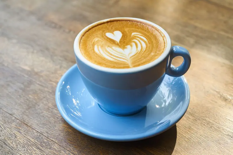 A beautifully crafted latte with heart-shaped art in a blue cup on a wooden table