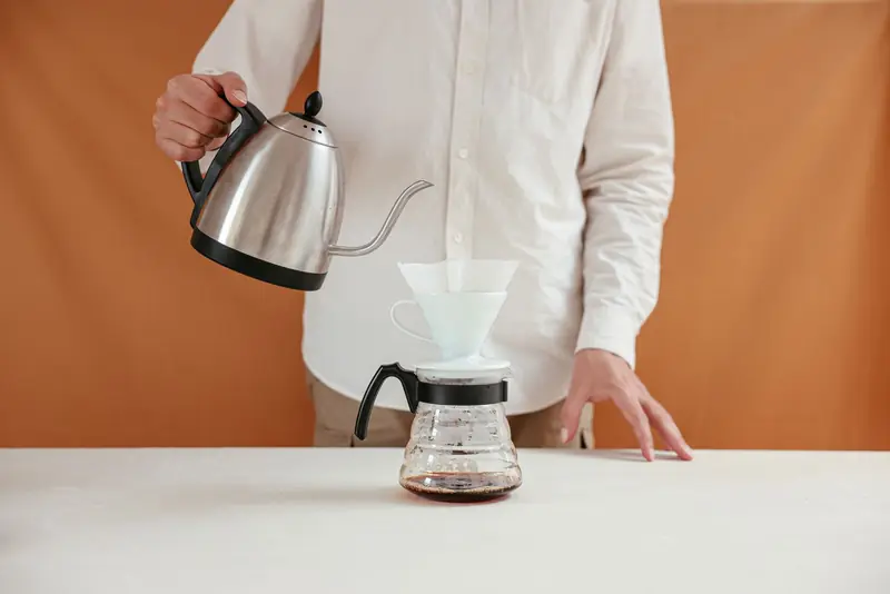 A person brewing pour over coffee using a dripper and kettle in a minimalistic setting